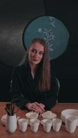 Elegant businesswoman in a black suit sitting at a wooden table with a tea set, posing for the camera in slow motion, with subtle changes in expression and posture video