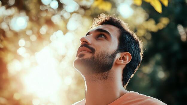 Man gazes upward at sunlight filtering through trees in a natural setting during late afternoon photo