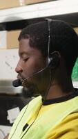 Vertical Male call center clerk assisting a person with order mix up problems, verifying parcel status on package tracking software in the warehouse facility. Customer service dispatch support. Camera A. video