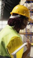 vertikal afrikansk amerikan arbetare ser till paket status på en paket spårning programvara på pc, arbetssätt i industriell depå för importera exportera operationer. hantera lager och avsändande protokoll. kamera a. video
