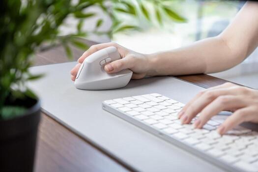 Female hand using a white vertical ergonomic mouse on a grey desk pad with a keyboard, emphasizing comfortable computing and productivity in a modern work environment photo