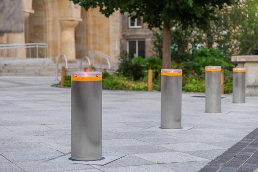 A row of modern retractable security bollards with red indicator lights standing on a paved urban square for public access control and safety photo