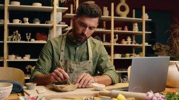 caucasico uomo maschio tipo piccolo attività commerciale la creazione di artista artigiano vasaio parlando in linea il computer portatile computer insegnamento ceramica scolpire utilizzando attrezzo in linea ceramica lezione e-learning passatempo sviluppo a laboratorio video