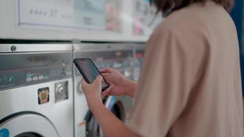 en modern scen utvecklas som en person användningar en smartphone till fungera en tvättning maskin symboliserar de genomskärning av varje dag uppgifter med digital teknologi. video