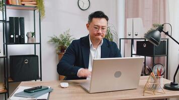 irritado cansado asiático negocio hombre mientras trabajando en computadora portátil, inesperado en línea sitio web problema, computadora virus datos pérdida por hackear. persona de libre dedicación sensación enojado acerca de roto cuaderno a oficina lugar de trabajo video