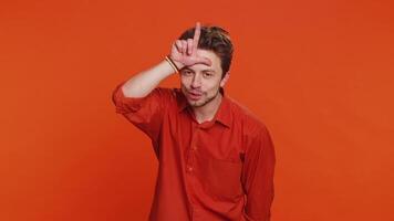 Caucasian man showing loser gesture and pointing on you, blaming accusing for unsuccess, expressing disrespect, mocking your failure, bullying abuse. Young guy isolated on orange background indoors video