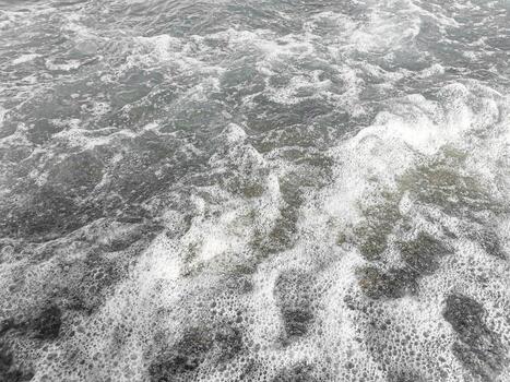 Sea waves crashing on rocky shore creating foam and ripples in a dynamic water scene photo