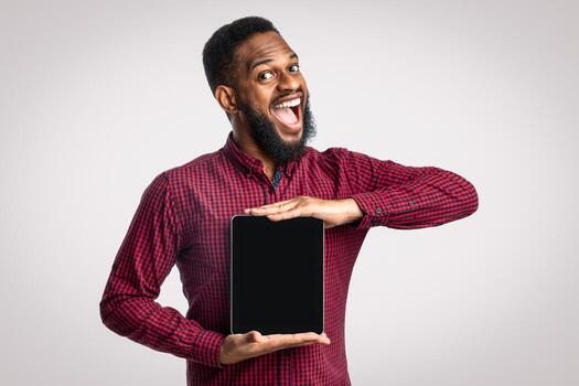 solicitud anuncio publicitario. emocionado africano hombre demostración digital tableta blanco pantalla recomendando aplicación o sitio web posando terminado blanco estudio fondo, sonriente a cámara. tecnología y en línea Servicio foto