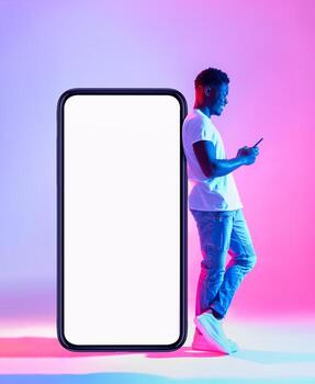 Full length of young black man using mobile phone while leaning on huge smartphone with empty white screen in neon light. Mockup for cool new app or website, space for ad photo