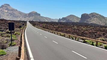 A stunning road winds through a unique volcanic landscape, surrounded by majestic mountains under clear skies video