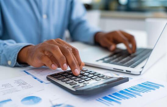 Close-up of person using calculator and laptop at desk photo