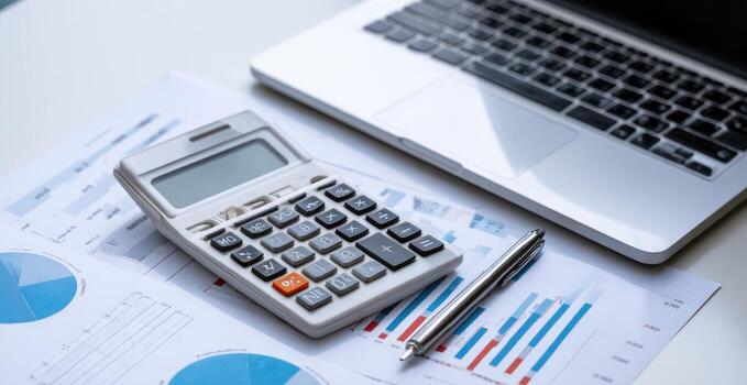 Calculator, laptop, and charts on a white surface photo