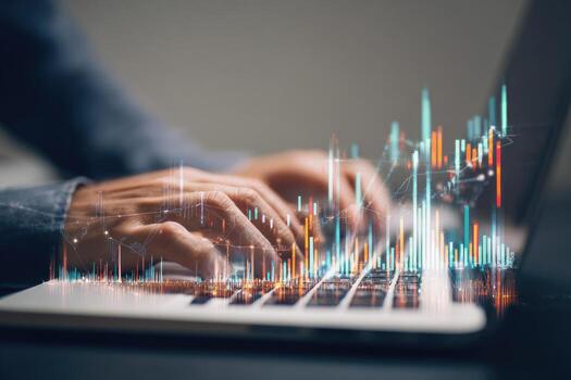 Hands typing on a laptop with stock market graphs overlayed photo