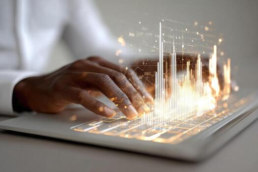 Close-up of hands typing on a laptop with glowing financial charts overlay photo