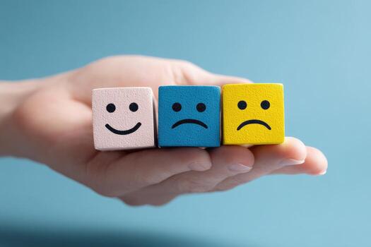 Hand holding three small wooden blocks, each with a different facial expression happy, sad, and sad photo