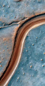 High-angle view of a winding, reddish-brown channel on a light-blue, textured surface. Speckled with golden-orange dots photo