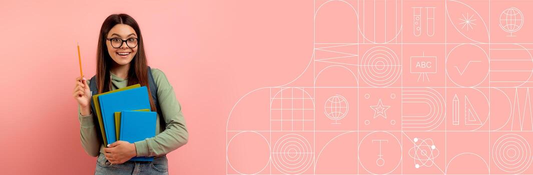 A cheerful student is holding a stack of blue books while excitedly posing. The background features a soft pink color with educational elements, providing an inviting atmosphere for studying. photo
