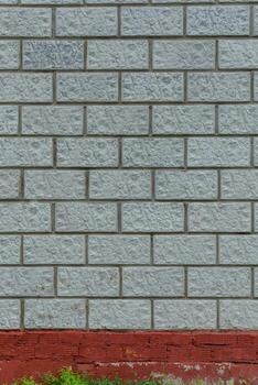 Light gray brick wall with a staggered pattern and rough surface. A red painted section and green vegetation create contrast at the base. photo