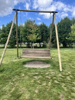 Wooden swing with ropes standing on green grass in a sunny park with trees and blue sky background photo