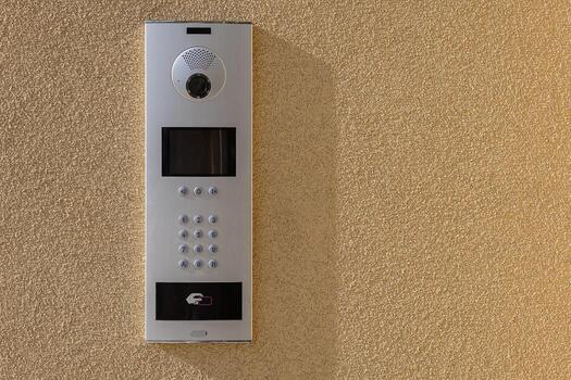 Modern intercom system with a built-in camera, keypad, and contactless access control panel mounted on a textured beige wall. Security, smart home technology and controlled building entry photo