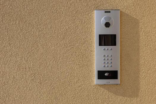 Modern intercom system with camera, keypad and RFID access on textured wall in sunlight. Security technology for residential and commercial buildings, ensuring controlled access and communication photo