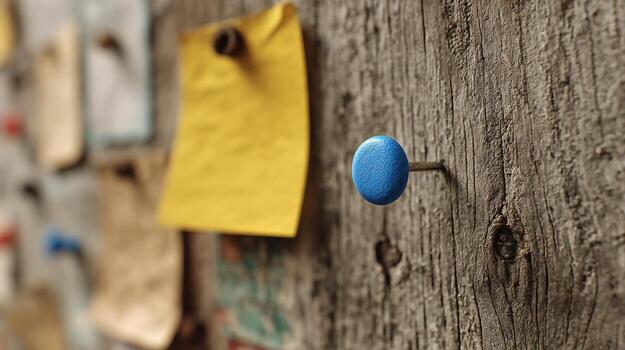 Close-up of a blue pushpin on a weathered wooden surface with a blurred background of papers and notes photo