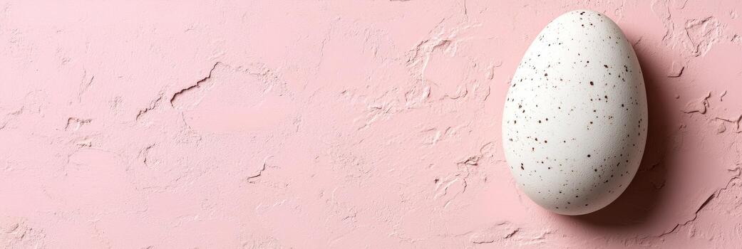 Unique speckled egg resting on a soft pink background with texture and subtle details photo