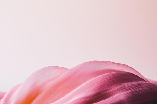 Soft pink fabric gently draping over a surface with a smooth gradient background in a soft light setting photo