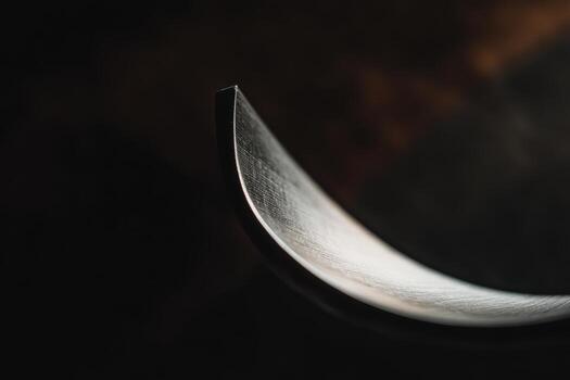 Close-up view of a curved metal blade reflecting light in a dark setting photo