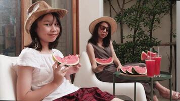 Chilling Asian family holidays, casual girl and mum enjoy eating pieces of fresh red watermelons sliced and smoothie drinks, happiness relaxing on vacation, and hot summertime at outdoor terrace. video