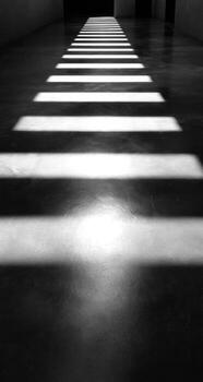A black and white photo of a long hallway with light coming from the windows