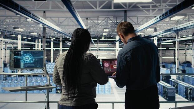 Team of server room technicians alerted by warning message on laptop causing infrastructure slowdowns. Teamworking data center colleagues see malfunction popup caused by software errors, camera A photo