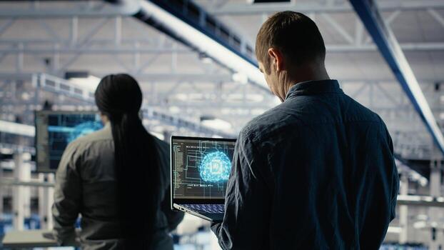 Data center system administrators investigate neural networks configuration, adjusting for optimal function. Server hub employees use laptop to check deep learning error reports, camera B photo