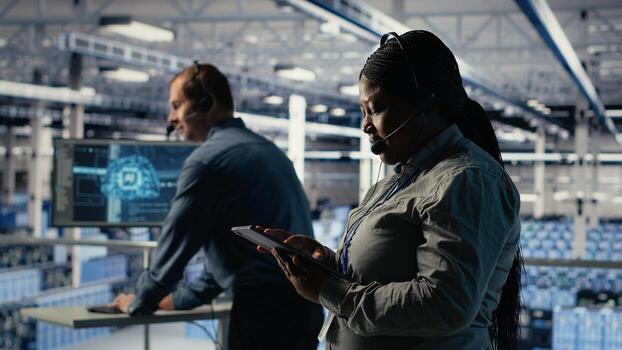 Data center system administrator uses AI on tablet to help customers resolve website hosting problems. African american woman in server farm helps users keep online services running smoothly, camera B photo