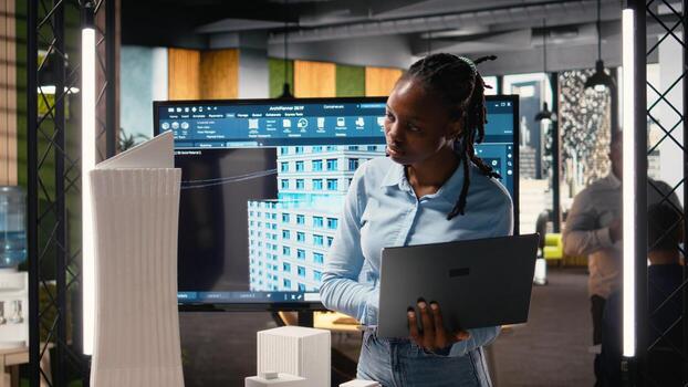 African american female evaluating 3D building model for measurements, creating construction blueprints for layout and preparing documentation for approval on a residential project. photo