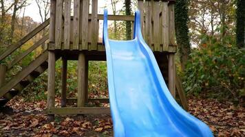 ein Blau rutschen befestigt zu ein hölzern Spielhaus Struktur im ein Park mit Herbst Blätter um es video