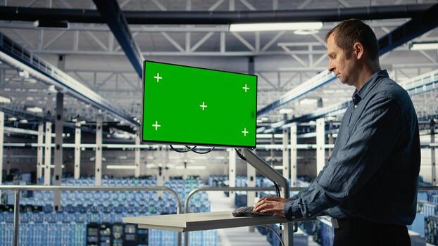IT expert monitors server farm activity using green screen workstation. Data center system administrator reviews rigs tests results on mockup display to ensure systems are working correctly, camera A photo