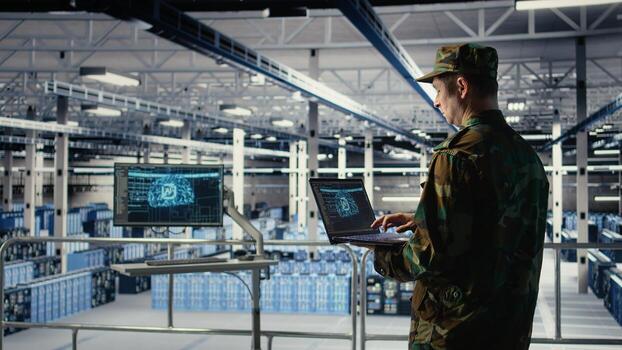 Soldier in engineering role uses AI application on laptop to manage server hub systems. Army commander reviews secret intelligence information using artificial intelligence in data center, camera A photo