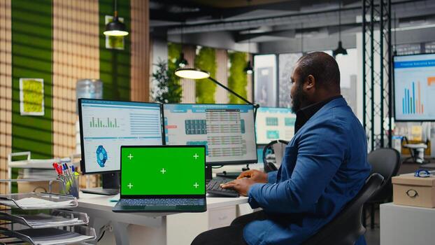 Black analyst uses computer to analyze charts with chroma key on laptop, preparing strategy reports to improve business management efficiency and achieve objectives for development. photo