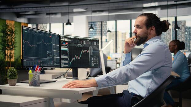 Trader in office expresses concern as investment portfolio value declines after unexpected market events. Financial professional stressed while reviewing stock exchange account losses photo