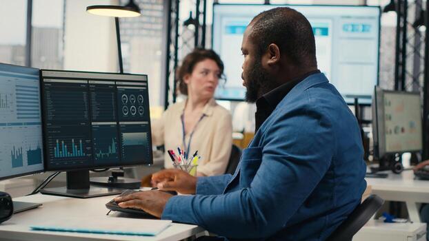 Black male administrator in modern workspace analyzing forecast insights and business strategy on a computer monitor, ensures report writing and planning for productivity. photo