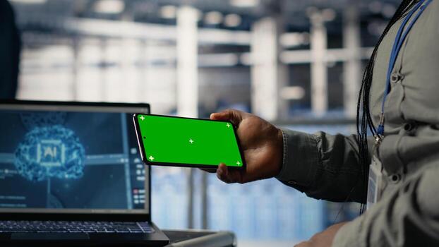 Data center worker uses green screen smartphone while deploying deep learning software. Server hub employee uses mockup mobile phone while training AI systems with datasets photo