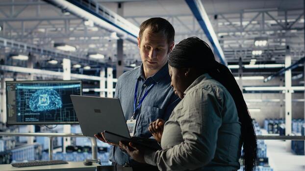 Team of data center programmers monitors deep learning process with laptop, reviewing operational metrics. Teamworking server hub colleagues review neural networks reports during inspection, camera B photo