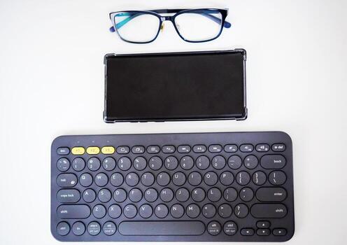 Minimal Workspace with Wireless Keyboard, Smartphone, and Glasses on White Background photo