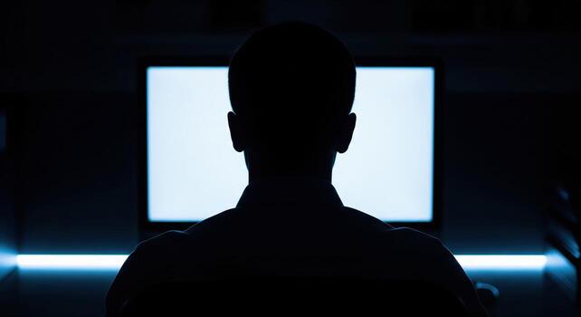 Anonymous Person Silhouette Working on Computer Screen in Dark Room photo