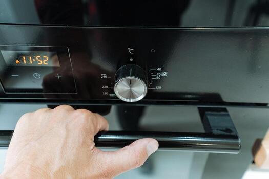 A closeup image capturing a hand reaching out for the control knob on a sleek, black kitchen oven, which elegantly showcases both its modern design and impressive functionality for cooking tasks photo