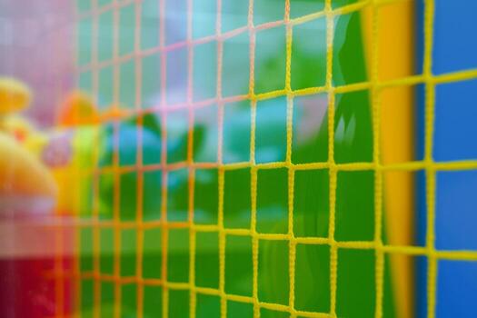 A vibrant mesh grid with yellow lines intersects colorful backgrounds of green and blue. Soft toys are visible through the grid, creating a playful ambiance. photo