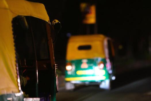 Auto rickshaws illuminated by streetlights, navigating through a nighttime urban environment while showcasing transportation dynamics. photo