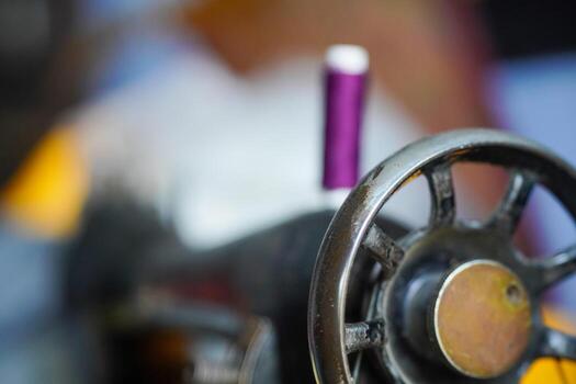 Side profile of an old sewing machine with purple thread, highlighting the wheel and handle mechanism from a close-up angle photo