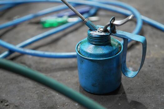 Blue oil can and hose placed on the floor of a workshop, surrounded by tools and parts. photo